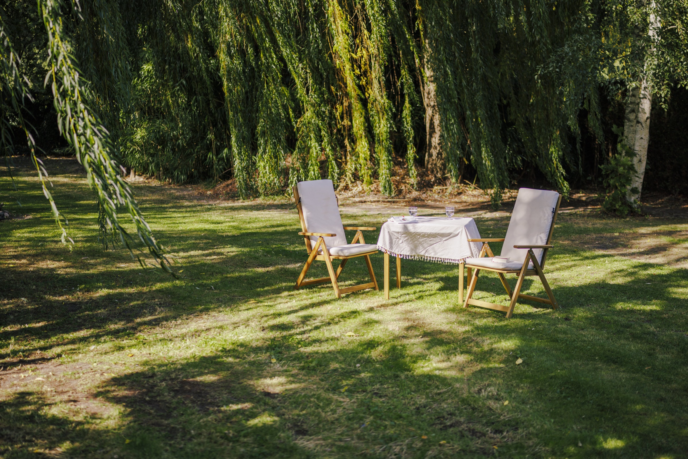 Gartentisch mit zwei Stühlen unter Weiden