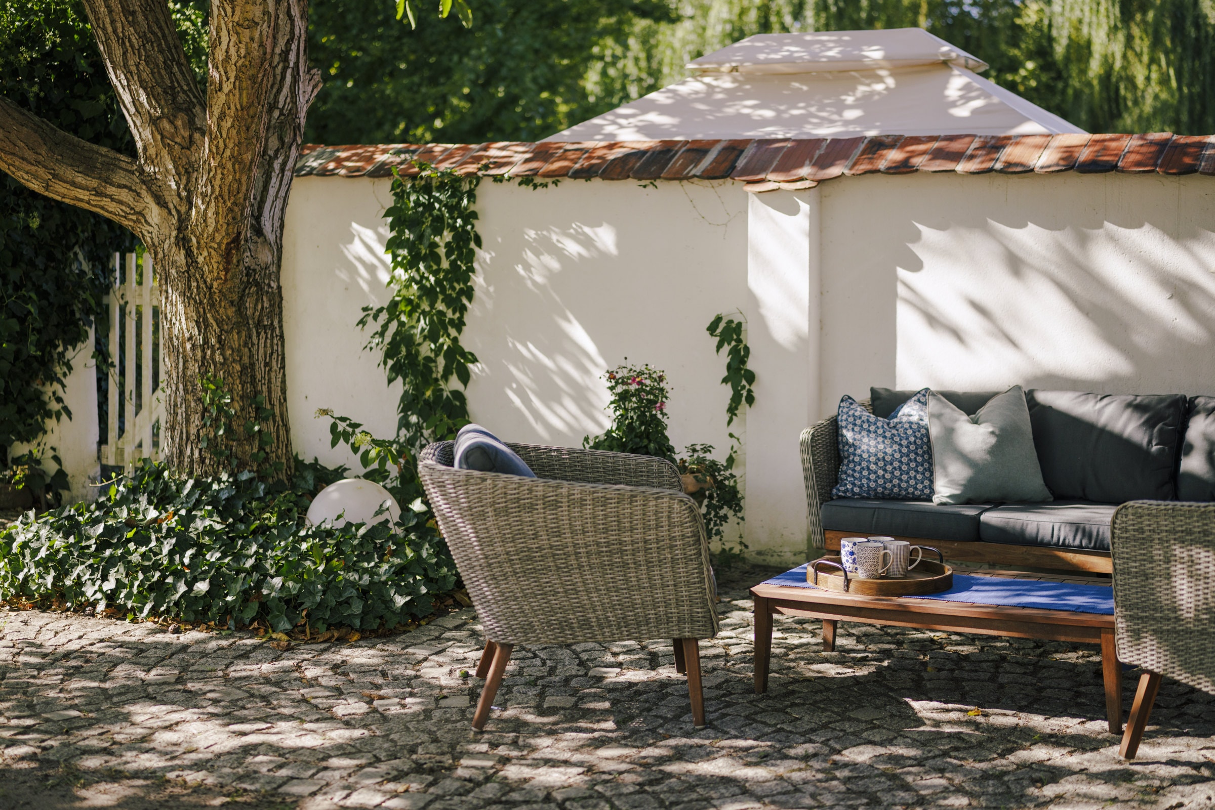 Lounge-Ecke mit Korbsofa unter einem alten Baum